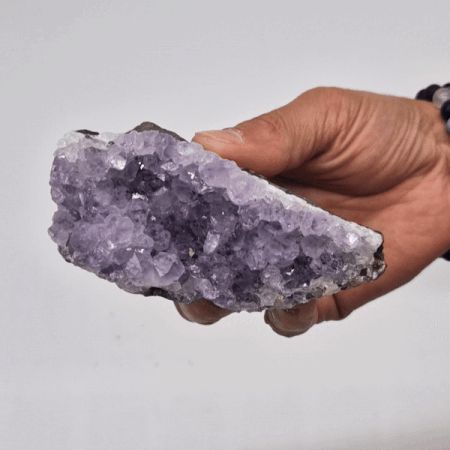 Hand holding a large purple crystal against a plain background